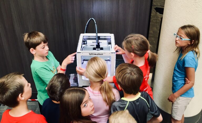 children sitting on chair in front of a 3D printer